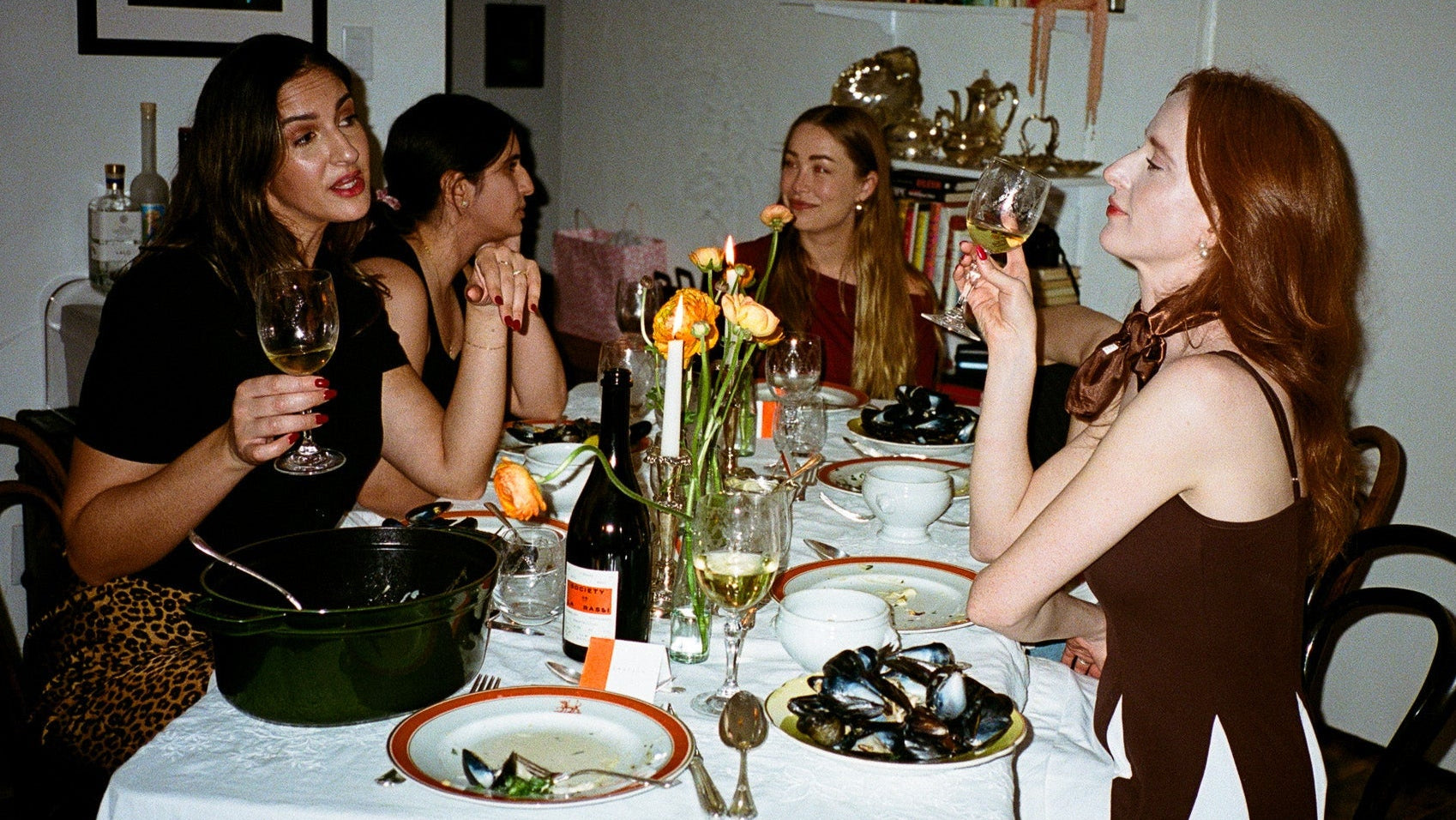 Group of women sitting around a dinner table with food and drinks.