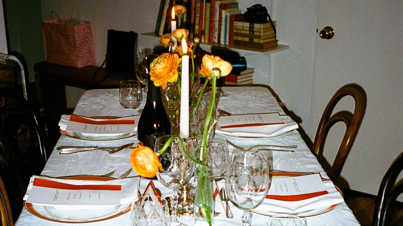 Dining table set with white tablecloth, orange napkins, and floral centerpieces.