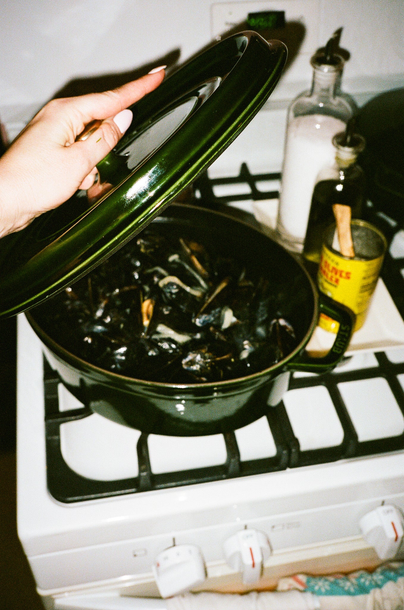 Person opening a green pot on a stove with mussels inside