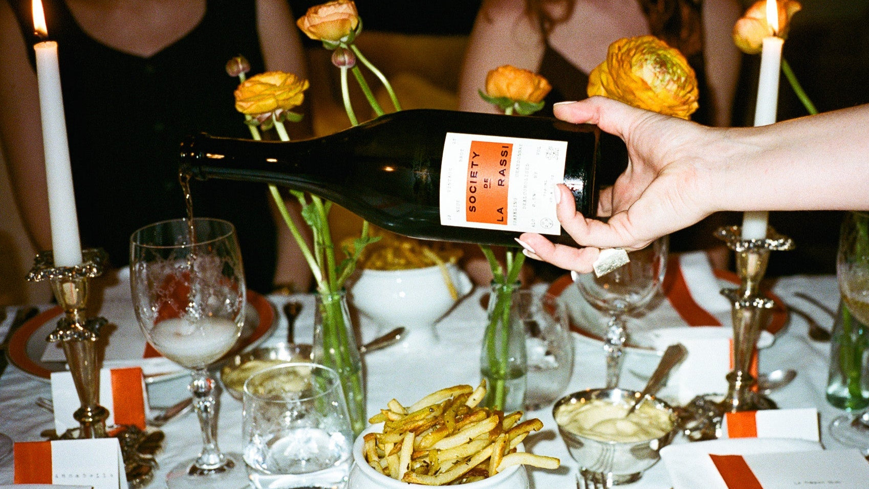 Person pouring wine at a dinner table with candles and floral arrangements.