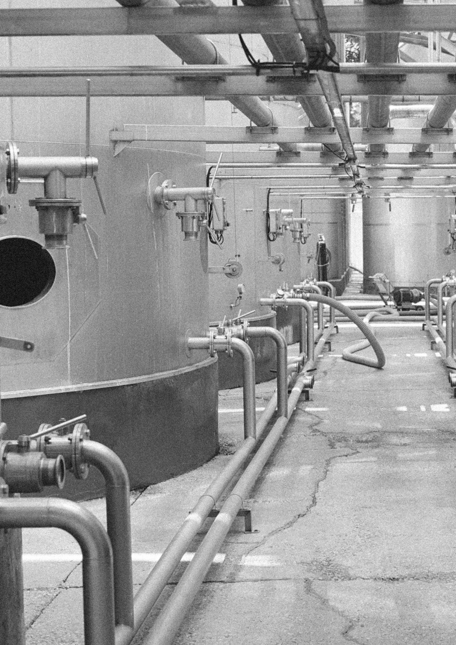 Industrial setting with large cylindrical tanks and pipes in a black and white photograph.