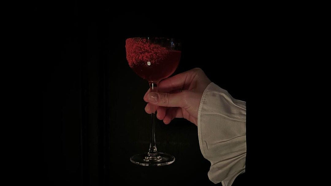 Hand holding a glass of red wine against a black background