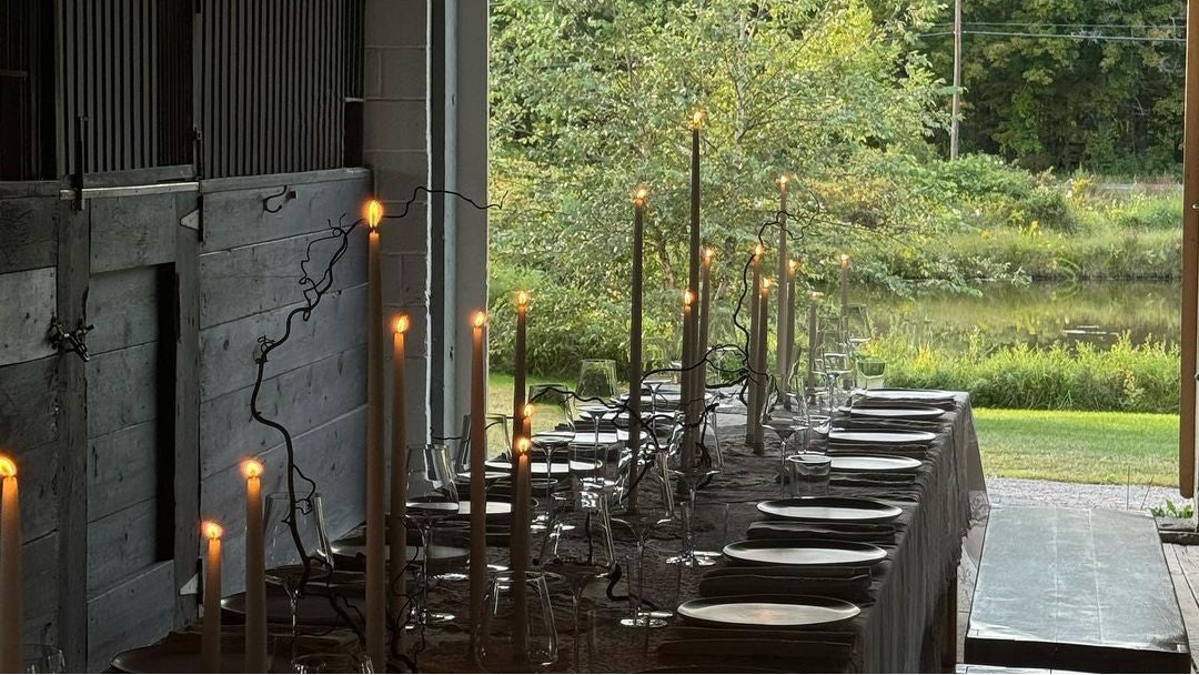 Long dining table set with candles and plates by a large window with a view of greenery.
