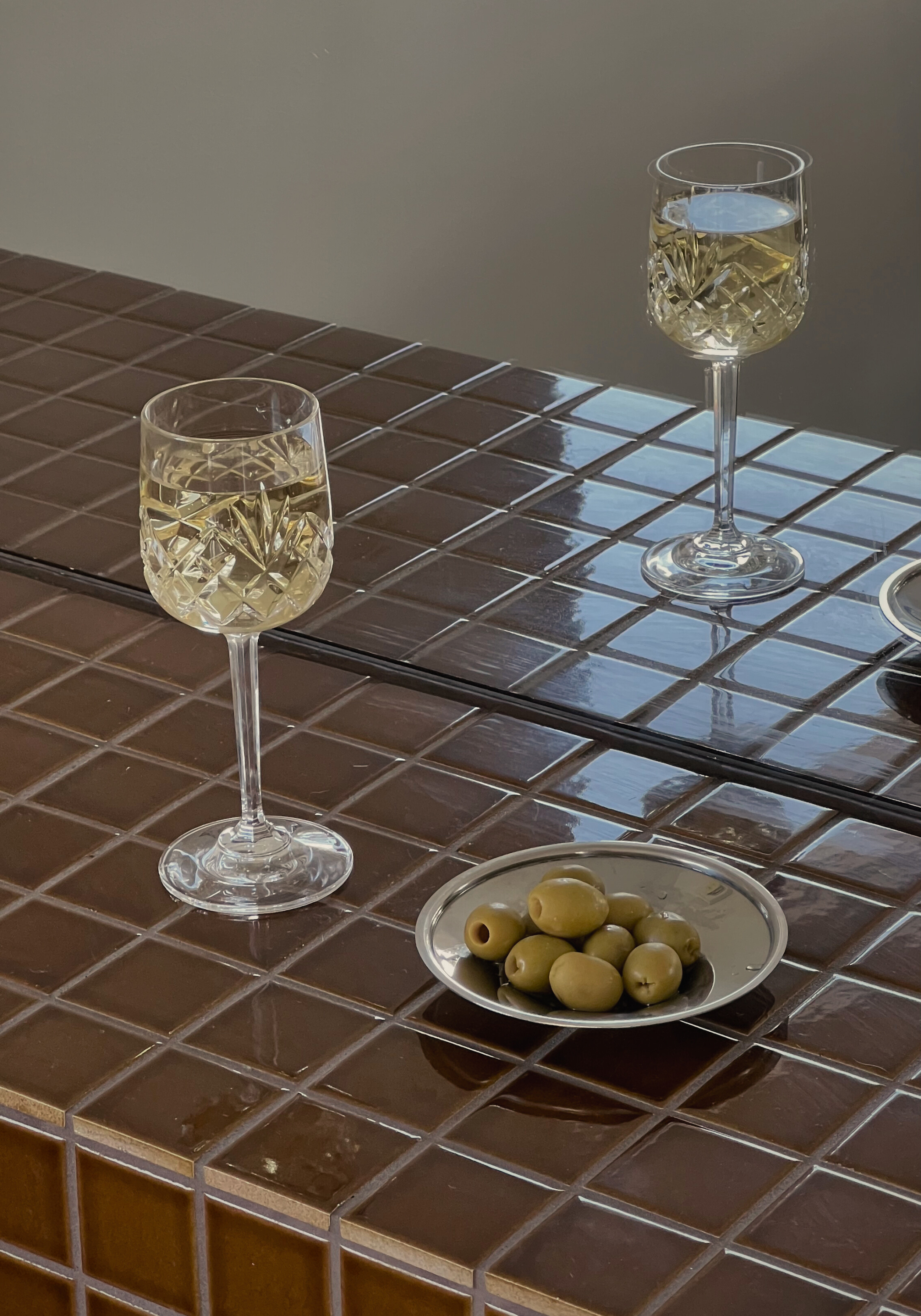 Two glasses of white wine on a tiled table with a small plate of olives.