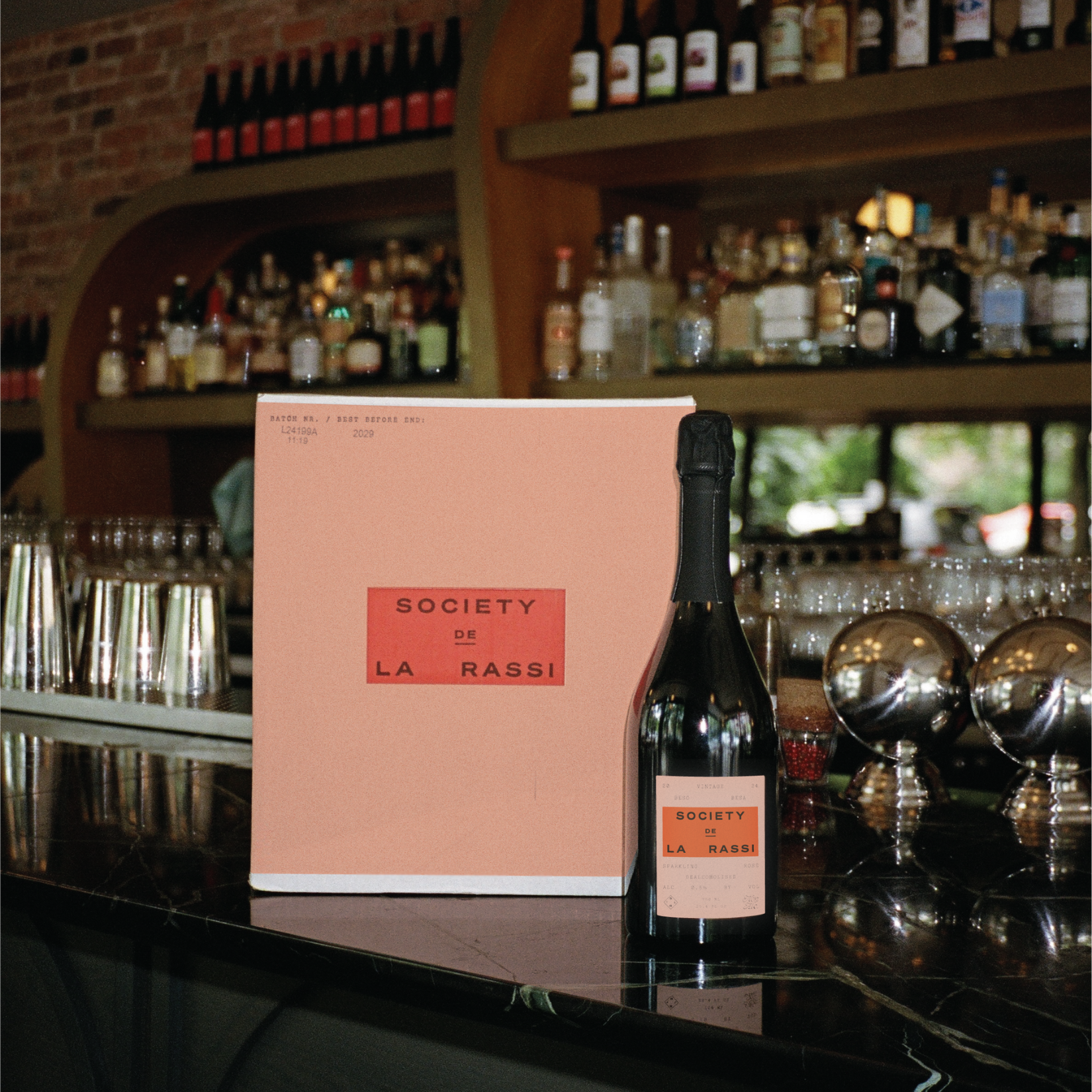 Bottle of Society De La Rassi Rose wine on a bar counter with a pink box in the background.