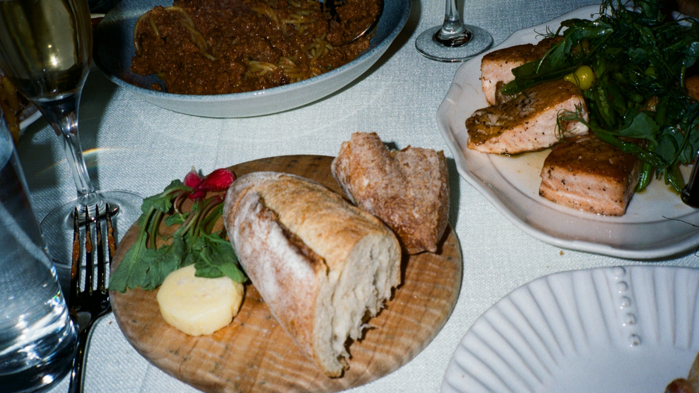 Table setting with bread, salad, and wine glasses on a white tablecloth.