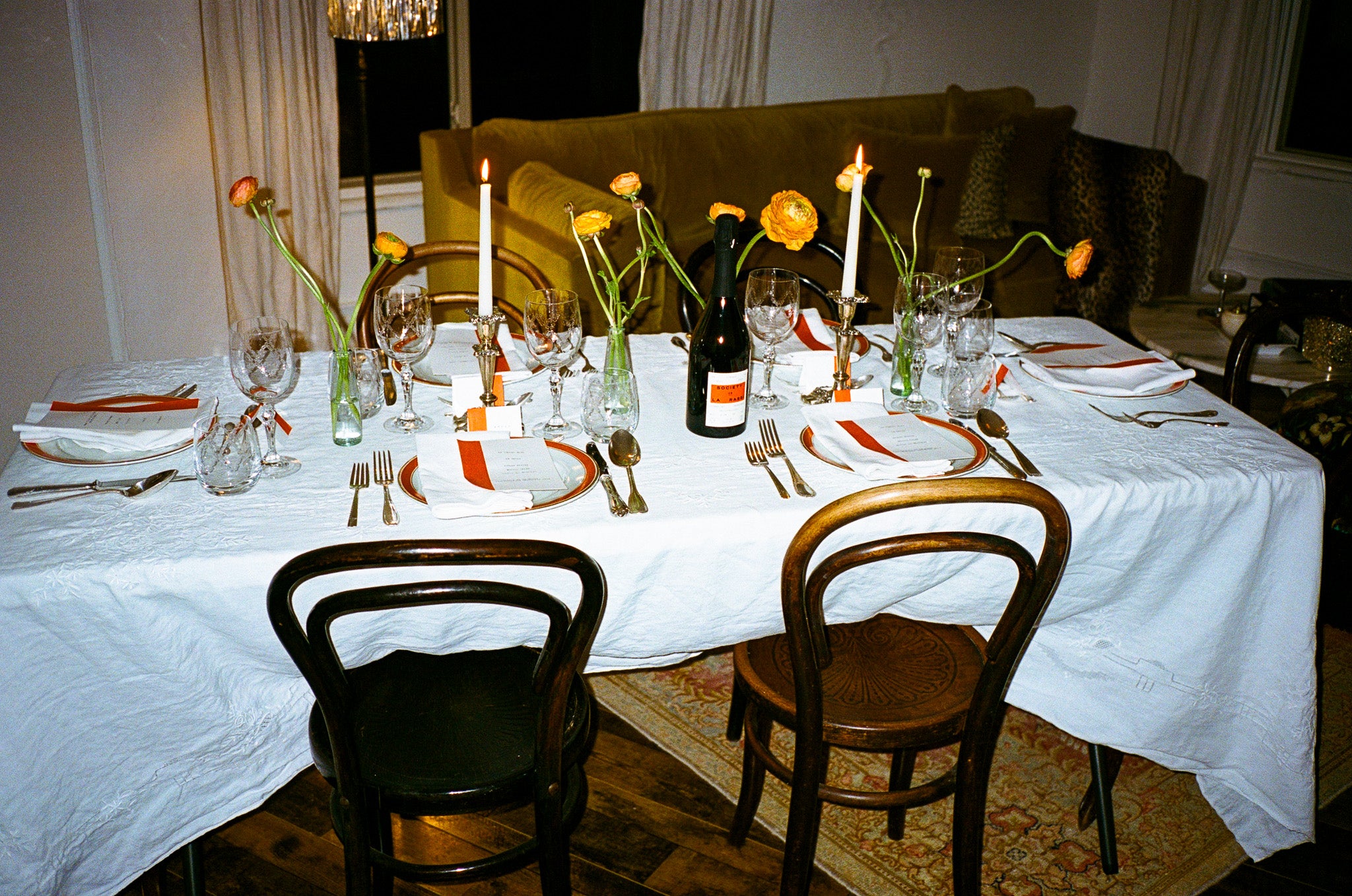 Dining table set for a meal with white tablecloth, wine glasses, and candles.
