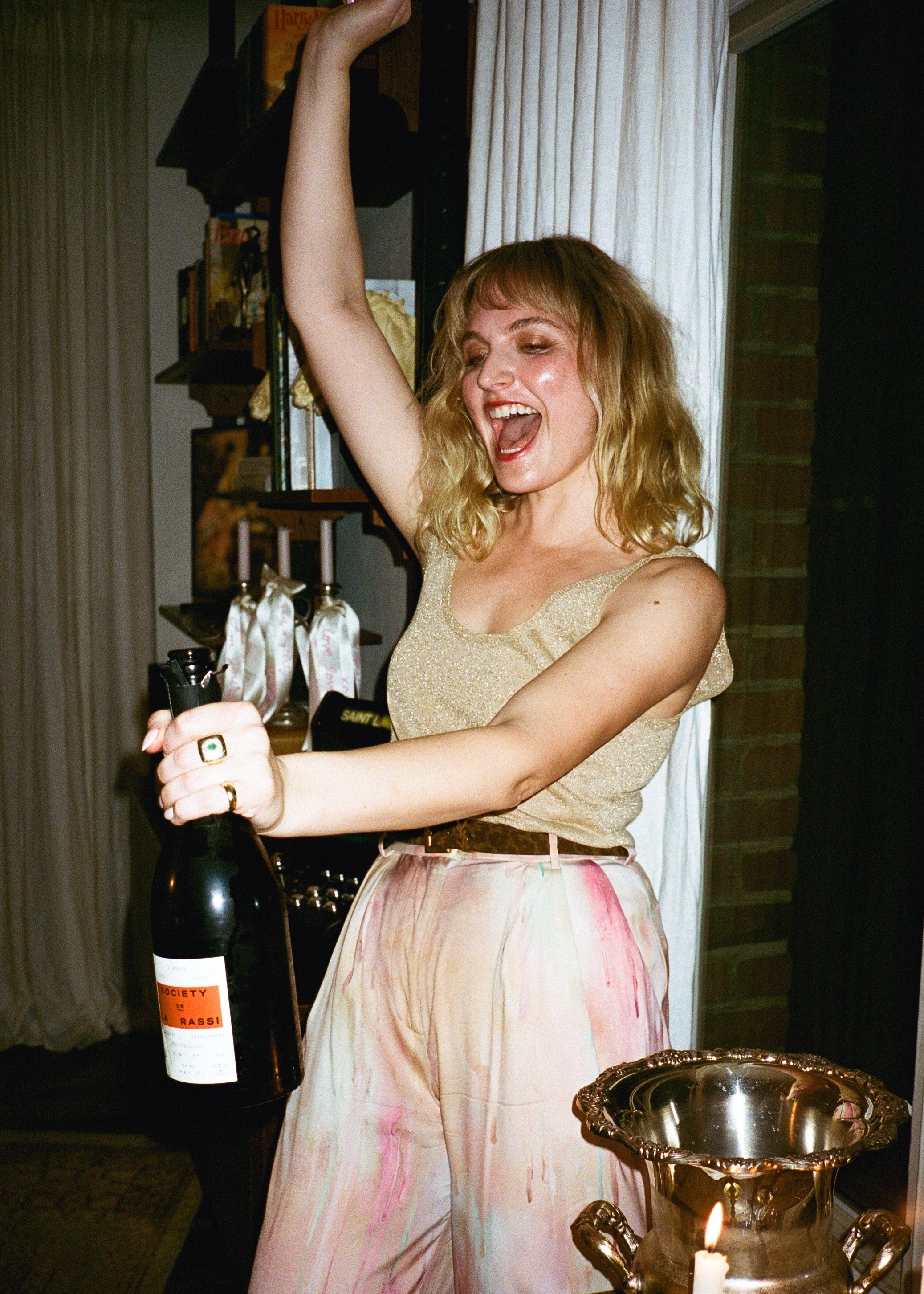 Woman in a celebratory pose while popping a bottle, indoors.