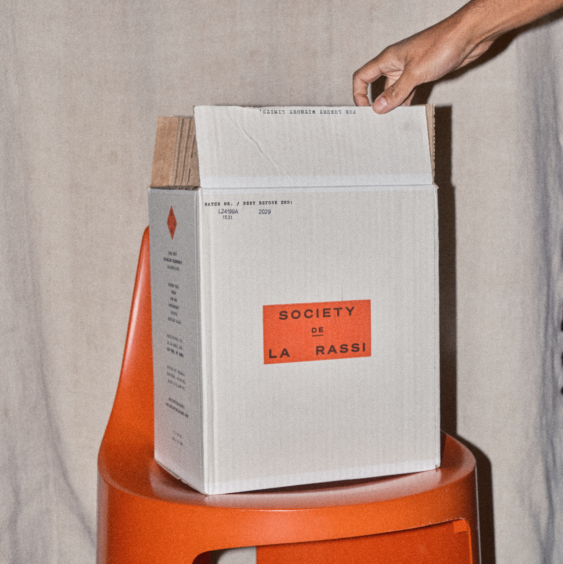 White box with 'Society de La Rassi' label on an orange stool against a beige background