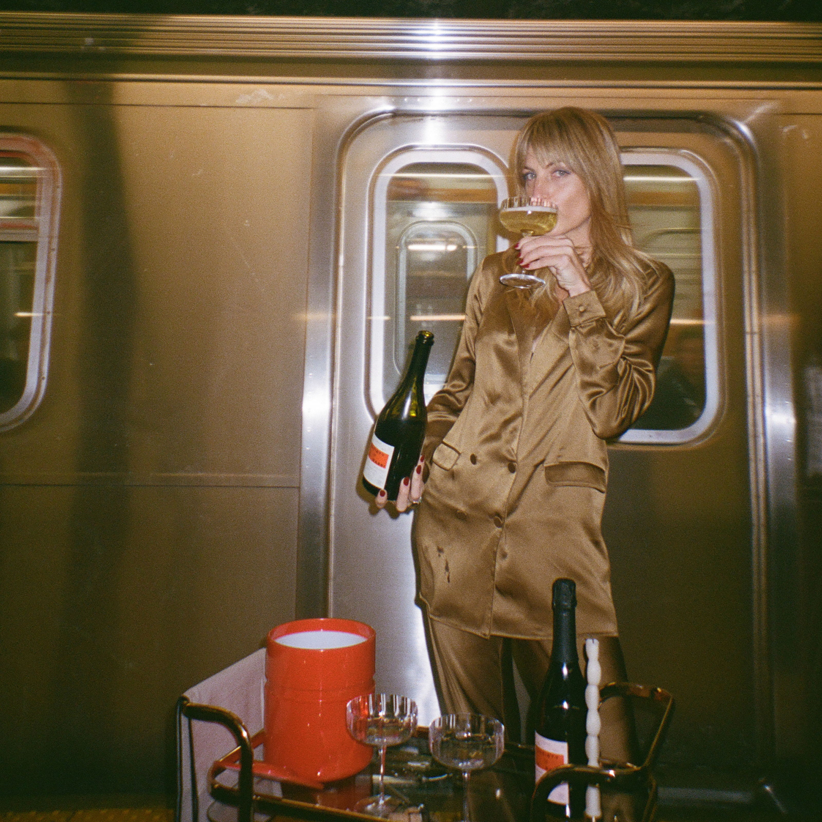 girl sipping glass of Non alcholic sparkling wine while NYC subway rushes behind