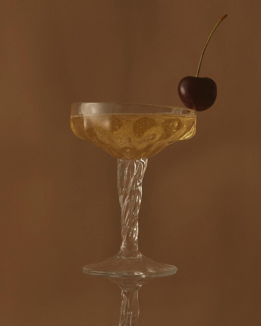 Cocktail in a glass with a cherry on a brown background