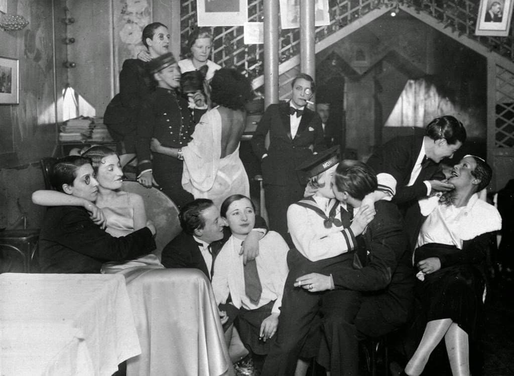 Vintage black and white scene of people in a crowded room, possibly a bar or theater.