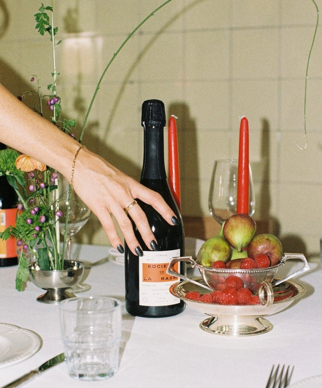 Hand placing a bottle of La rassi non alc sparkling on a table with red candles and white table cloth