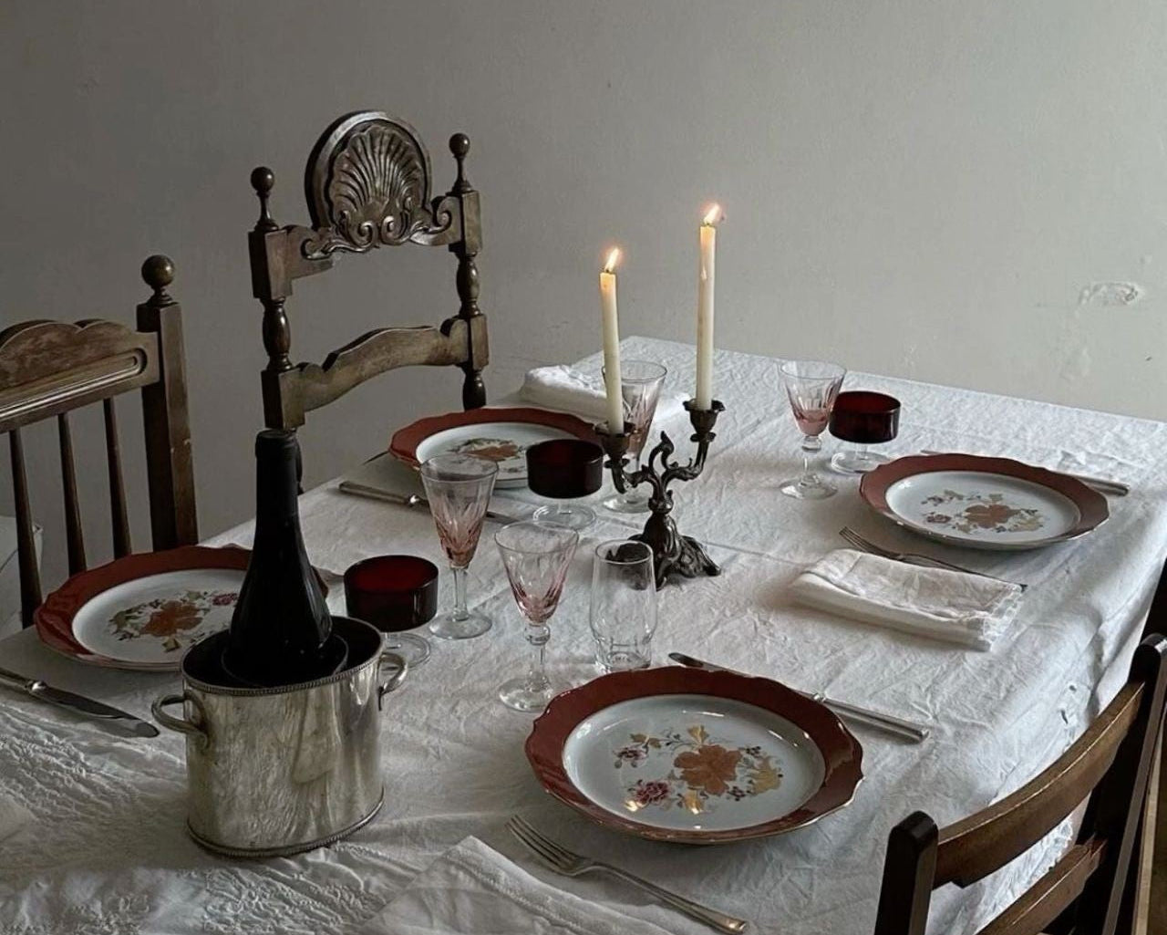 Dining table set with plates, glasses, and a bottle, with a candlelit ambiance.